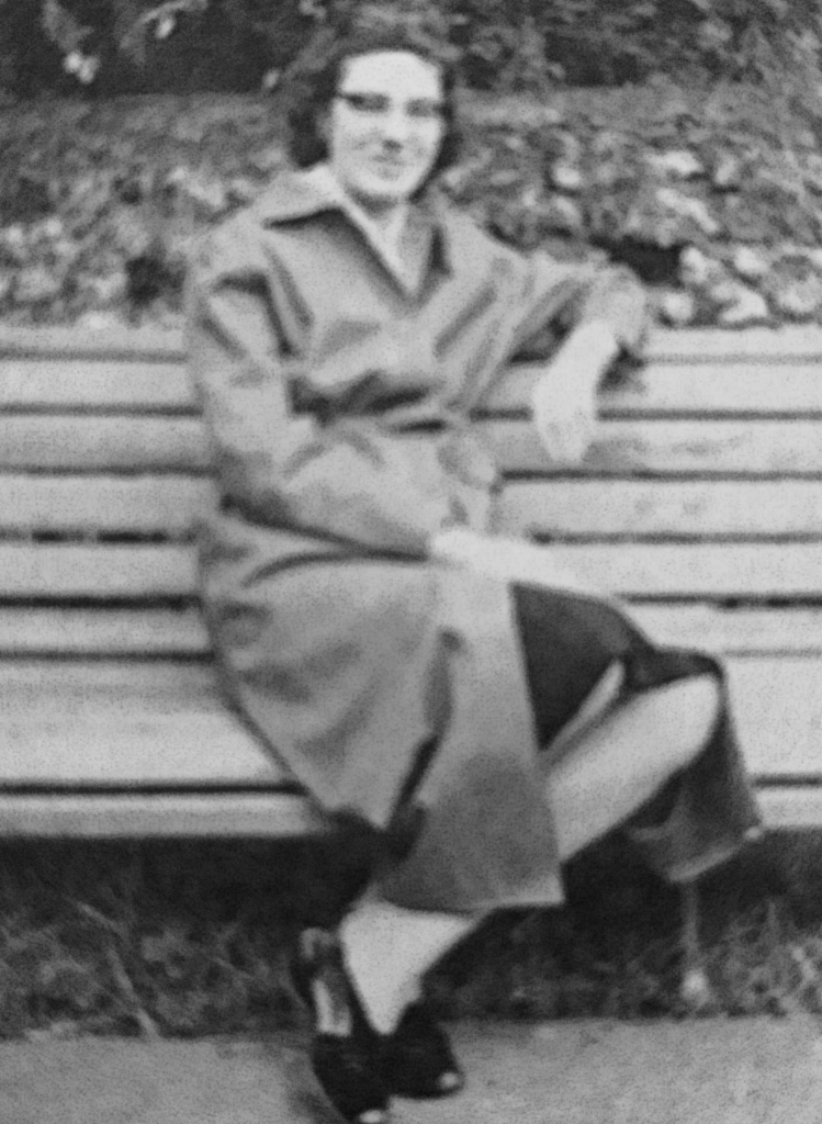 Young-Doreen-sat-on-a-park-bench-wearing-a-long-coat