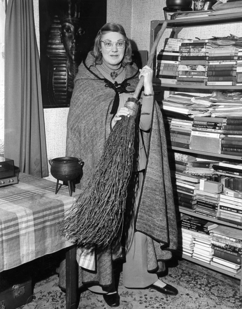 Young-doreen-with-cloak-and-broom-in-from-of-her-book